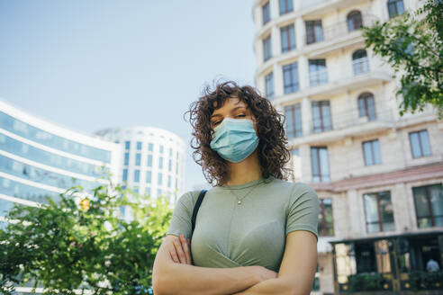 Brunette curly woman wearing protective mask in city - OYF00146