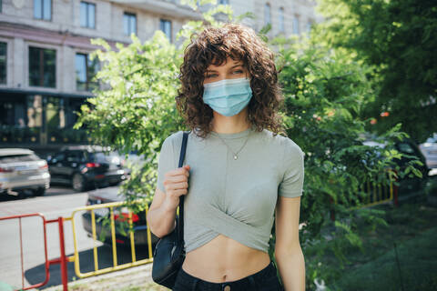 Brünette lockige Frau mit Schutzmaske in der Stadt, lizenzfreies Stockfoto