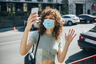 Woman wearing protective mask and using smartphone in city - OYF00148
