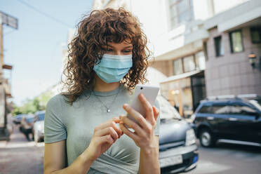 Woman wearing protective mask and using smartphone in city - OYF00150