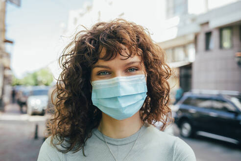 Brunette curly woman wearing protective mask in city - OYF00151