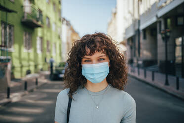 Brunette curly woman wearing protective mask in city - OYF00158