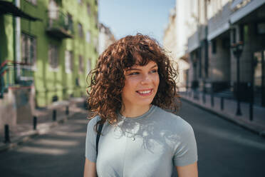 Porträt einer lächelnden brünetten lockigen Frau in der Stadt - OYF00159