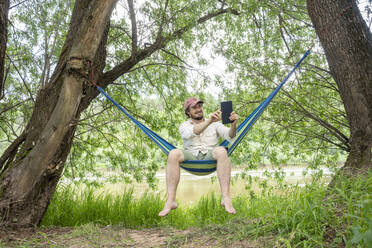 Man using tablet and sitting in hammock - VPIF02623