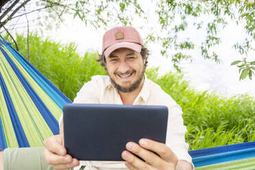 Mann benutzt Tablet und sitzt in der Hängematte - VPIF02624