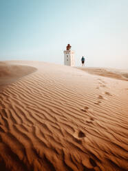 Rückansicht eines Touristen, der an einem Leuchtturm in den Sanddünen steht - ADSF04025