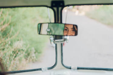 Reflection of young lady in rear-view mirror of retro car during trip in nature - ADSF04113