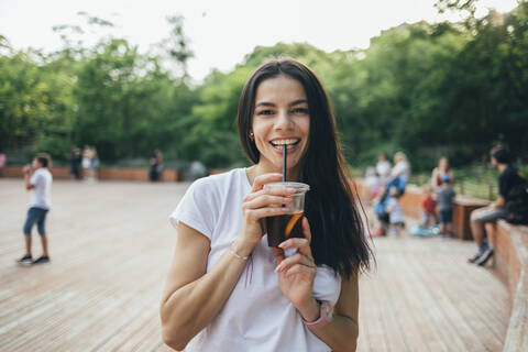 Glückliche junge Frau, die im Park stehend ein Erfrischungsgetränk trinkt, lizenzfreies Stockfoto