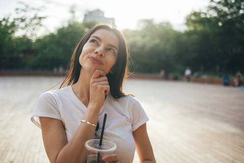 Close-up of thoughtful young woman with soft drink cup standing in park stock photo