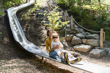 Mutter mit Tochter spielt auf einer Rutsche im Wald - DIGF12755