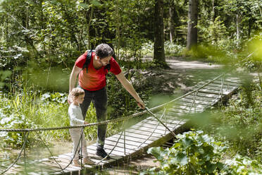 Vater und Tochter betrachten Pflanzen, während sie auf einem Steg im Wald stehen - DIGF12758