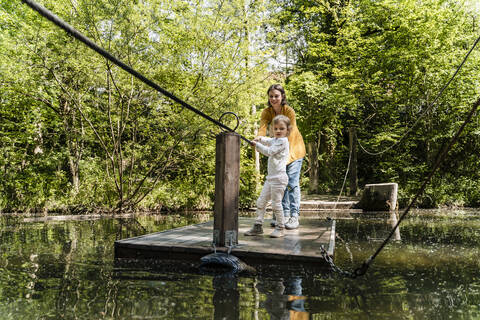 Mother and daughter standing on wooden raft over lake in forest stock photo