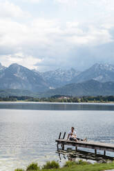 Vater mit Tochter sitzt auf dem Steg über dem See gegen Berge und bewölkten Himmel - DIGF12765