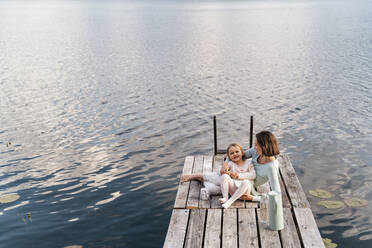 Mittlere erwachsene Frau und Tochter entspannen sich auf einem Steg über dem See - DIGF12771