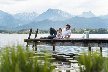 Vater mit Tochter entspannen sich auf einem Steg über dem See vor den Bergen - DIGF12772