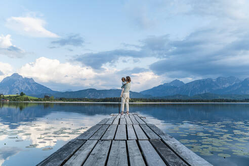 Mutter trägt ihre Tochter auf dem Steg über dem See gegen den Himmel - DIGF12789
