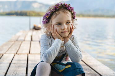 Nahaufnahme eines niedlichen Mädchens mit Diadem, das auf einem Steg am See sitzt - DIGF12792