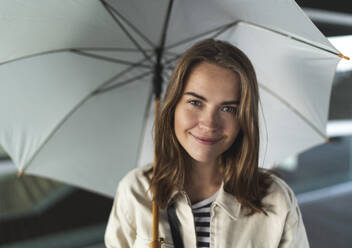 Close-up of happy young woman with umbrella standing in city - HPSF00037