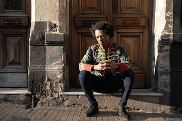 Confident male hipster sitting at doorway during sunny day - SPCF00761