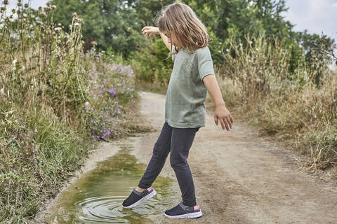 Girl playing with puddle while standing on dirt road stock photo