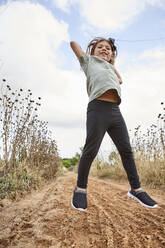 Cheerful girl jumping on land against cloudy sky - VEGF02535