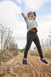 Fröhliches Mädchen springt auf Land gegen bewölkten Himmel - VEGF02535