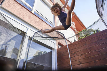 Verspieltes Mädchen springt auf Trampolin gegen Haus während sonnigen Tag - VEGF02538