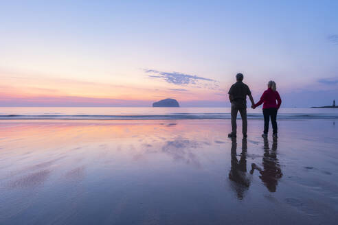 Paar schaut bei Sonnenuntergang am Seacliff Beach, North Berwick, Schottland, auf das Meer - SMAF01936