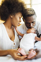 Close-up of man kissing newborn daughter held by mother at home - OCMF01527