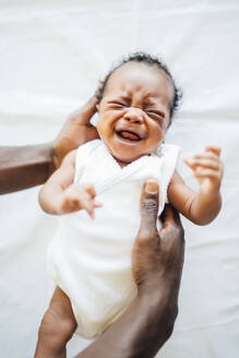 Close-up of father hands holding newborn daughter crying on bed at home - OCMF01528