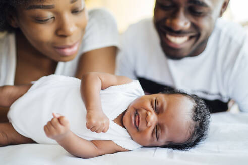 Nahaufnahme von lächelnden Eltern, die ihre neugeborene Tochter auf dem Bett schlafen sehen - OCMF01529