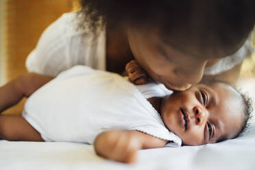 Nahaufnahme einer Mutter, die ihre neugeborene Tochter küsst, die zu Hause im Bett liegt - OCMF01535