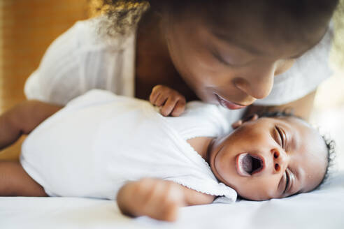 Close-up of mother looking at cute newborn daughter yawning while lying on bed - OCMF01536