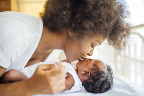 Close-up of mother kissing baby daughter lying on bed at home - OCMF01539