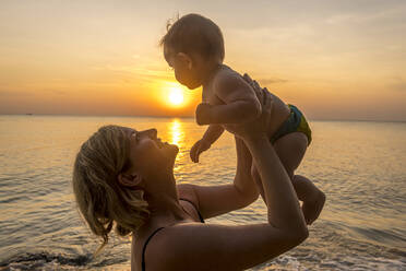 Vietnam, Phu Quoc island, Ong Lang beach, Mother holding baby in beach at sunset - RUNF03944