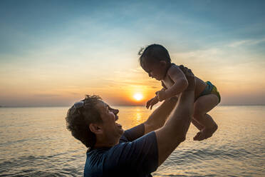 Vietnam, Phu Quoc island, Ong Lang beach, Father holding baby in beach at sunset - RUNF03947