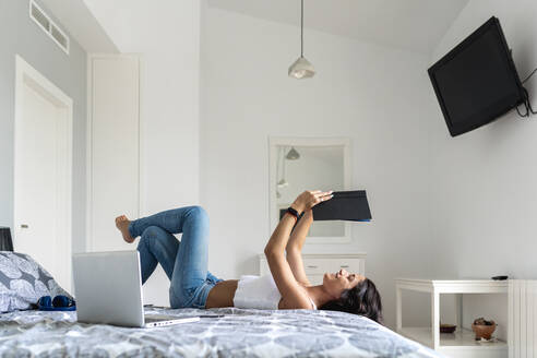 Mid adult woman reading book while lying on bed at home - EGAF00532