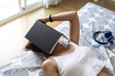 Mittlere erwachsene Frau mit Buch auf dem Gesicht entspannt im Schlafzimmer zu Hause - EGAF00534