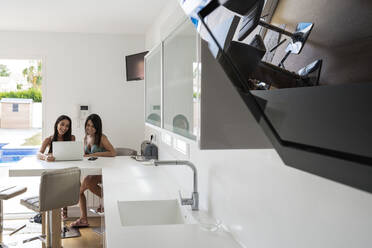 Freundinnen benutzen einen Laptop auf einem modernen Küchentisch zu Hause - EGAF00545
