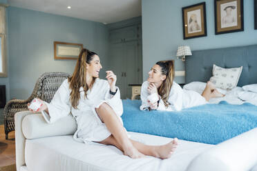 Cheerful twins sisters talking while relaxing in hotel room - OCMF01554