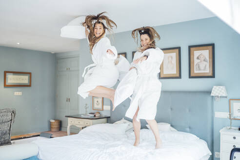 Cheerful twin sisters jumping on bed in hotel room - OCMF01561