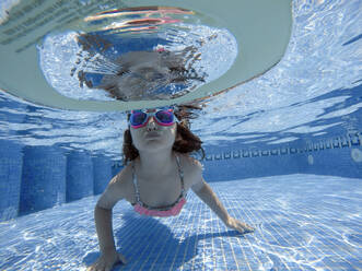 Nettes Mädchen mit Schwimmbrille schwimmt unter Wasser im Pool - EGAF00552