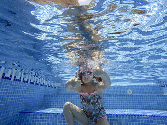 Mädchen zeigt Daumen hoch beim Schwimmen unter Wasser im Pool - EGAF00554