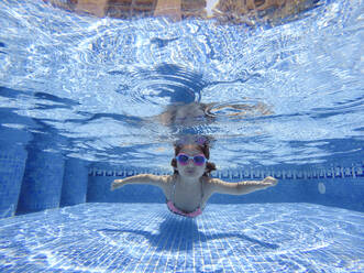 Mädchen schwimmt unter Wasser im Pool bei sonnigem Wetter - EGAF00555