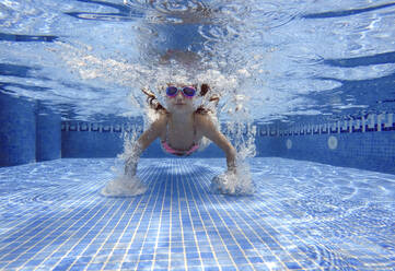 Mädchen mit Schwimmbrille taucht im Schwimmbad unter Wasser - EGAF00556