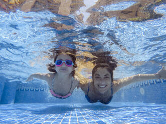 Happy mother and daughter swimming underwater in pool - EGAF00559