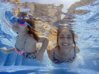 Lächelnde Mutter mit Tochter schwimmen unter Wasser im Pool - EGAF00560
