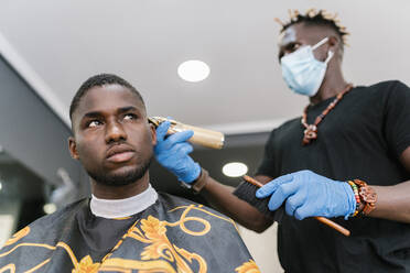 Friseur mit Maske und Handschuhen beim Schneiden der Haare eines Kunden mit einem Rasiermesser in einem Friseursalon - EGAF00563