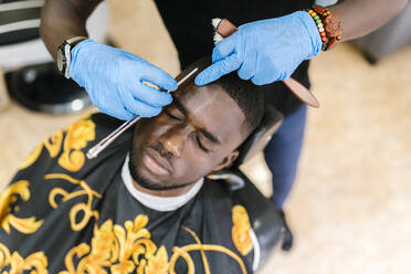 Nahaufnahme eines Friseurs mit Handschuhen, der die Haare eines Kunden mit einer Rasierklinge schneidet - EGAF00573