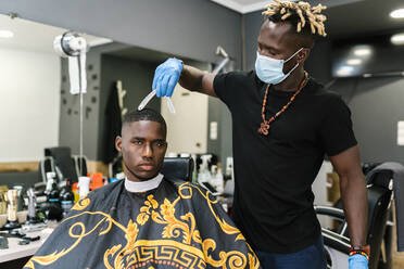Männlicher Friseur mit Salon und Handschuhen schneidet einem jungen Mann die Haare im Friseursalon - EGAF00576